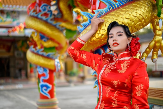 Asiatische schöne Frau des Porträts, die ein Cheongsam trägt, lächelt und posiert mit Gratulationsgeste am Schrein zum chinesischen Neujahr