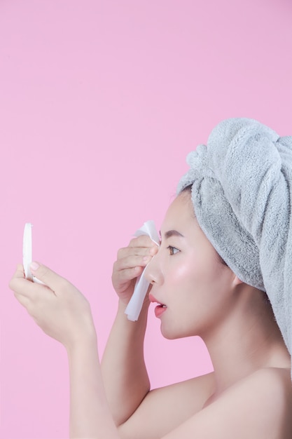 Asiatische schöne Frau säubert das Gesicht auf einem rosafarbenen Hintergrund.