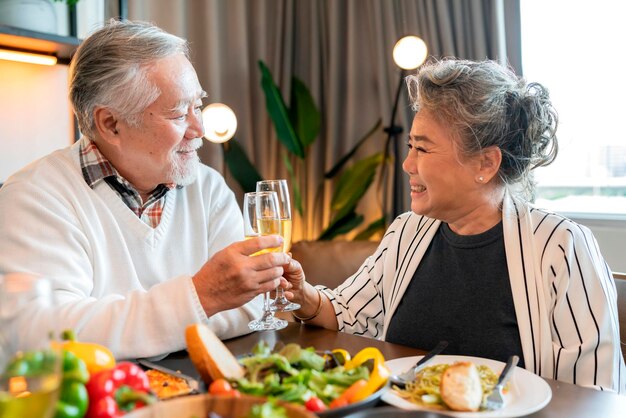 Asiatische Senioren-Seniorenglück fröhlichSchönes Seniorenpaar, das mit Gläsern Wein am Holztisch anstößt