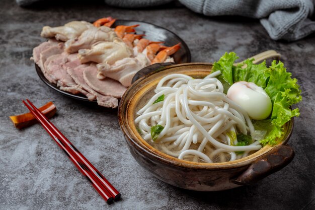 Asiatische Suppe mit Nudeln, Schweinefleisch und Frühlingszwiebeln dicht in einer Schüssel auf dem Tisch.