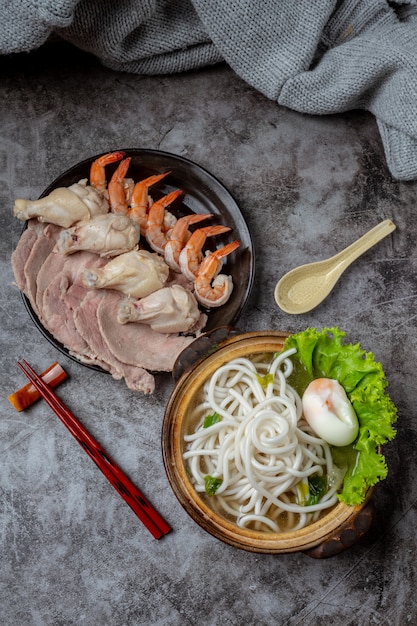 Asiatische Suppe mit Nudeln, Schweinefleisch und Frühlingszwiebeln dicht in einer Schüssel auf dem Tisch.