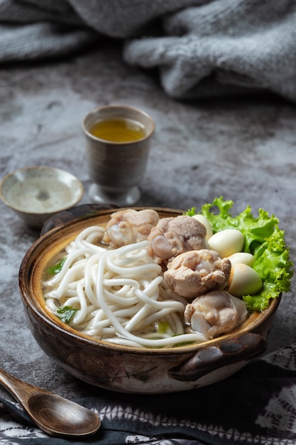 Asiatische Suppe mit Nudeln, Schweinefleisch und Frühlingszwiebeln dicht in einer Schüssel auf dem Tisch.