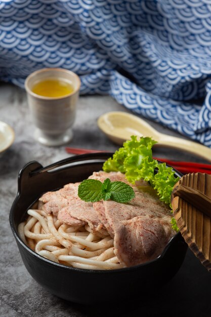 Asiatische Suppe mit Nudeln, Schweinefleisch und Frühlingszwiebeln dicht in einer Schüssel auf dem Tisch.