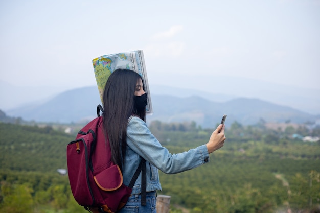 Asiatische Touristin mit Gesichtsmaske, die auf das Telefon schaut