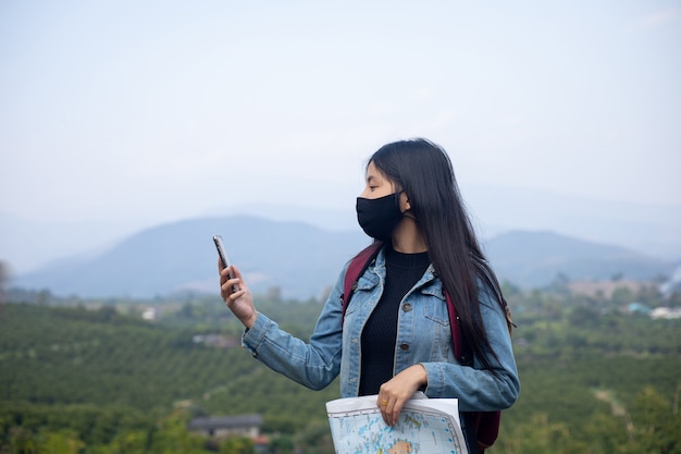 Asiatische Touristin mit Gesichtsmaske, die auf das Telefon schaut