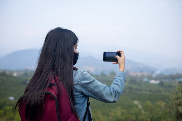 Asiatische Touristin mit Gesichtsmaske, die auf das Telefon schaut