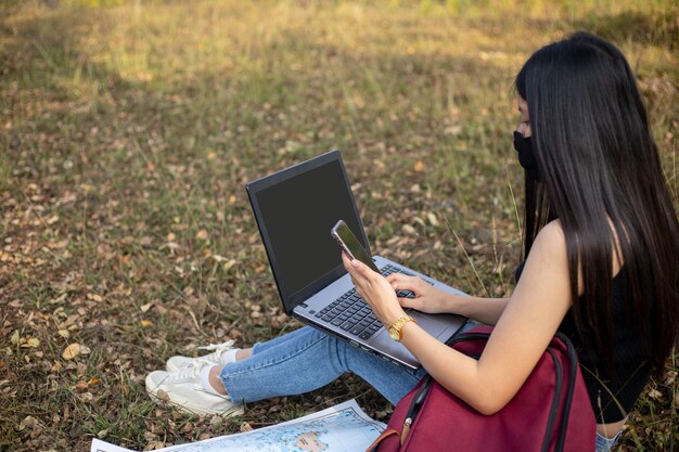 Asiatische Touristin mit Gesichtsmaske, die auf Laptop schaut