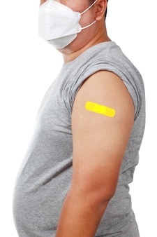 Asiatischer dicker mann, der eine weiße maske trägt und ein graues hemd trägt, der den linken arm mit gelbem pflaster zeigt, gegen covid-19 (coronavirus) geimpft auf weißem hintergrund. isoliert. beschneidungspfad