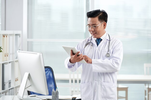 Asiatischer Doktor, der medizinische APP auf seinem digitalen Gerät verwendet