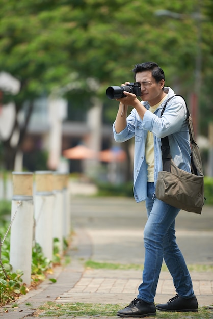 Asiatischer Fotograf mit der Berufskamera, die Fotos im städtischen Park macht