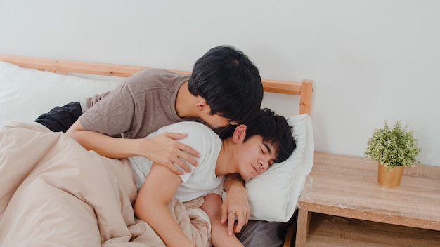 Asiatischer homosexueller Paarkuß und -umarmung auf Bett zu Hause. Junge asiatische LGBTQ + Männer, die glücklich sind, entspannen sich, verbringen zusammen romantische Zeit, nachdem sie morgens im Schlafzimmer zu Hause aufgewacht sind.