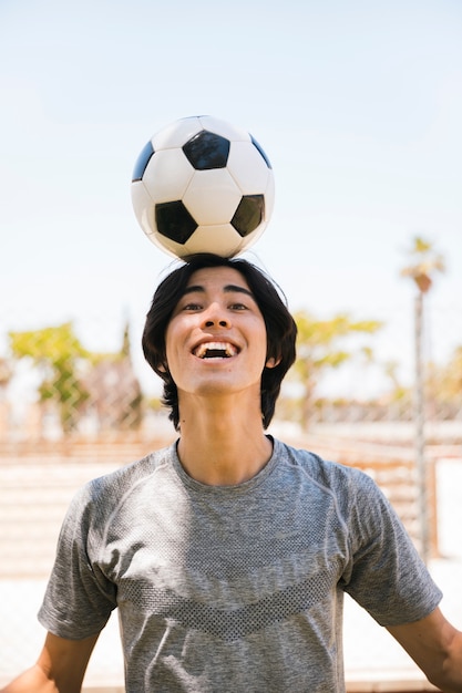 Asiatischer jugendlich Student, der Fußball auf Kopf hält