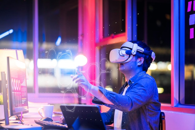 Asiatischer junger Mann mit tragbarem Goggle-Headset virtueller Online-Meeting-Digitalraum, der mit erweiterter 3D-Dimension zu Hause arbeitetCyber-virtuelles Arbeiten mit virtueller VR-Brille und PC-Desktop-Gerät
