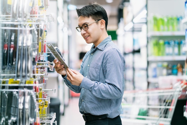Asiatischer kunde männlich einkaufen wählen produkt aus dem regal im hintergrund des einkaufszentrums