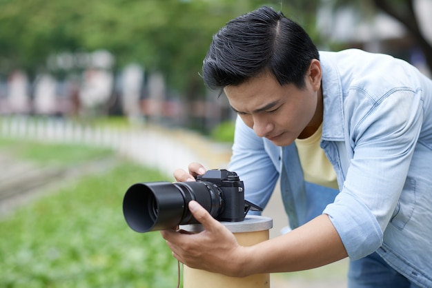Asiatischer männlicher Fotograf, der Kamera im städtischen Park gründet