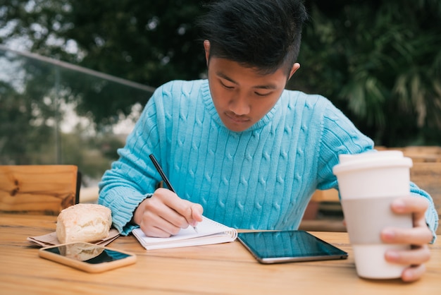 Asiatischer Mann, der digitales Tablett verwendet und Notizen macht