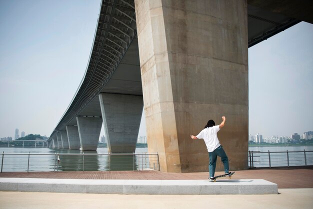 Asiatischer Mann, der draußen in der Stadt Skateboard fährt