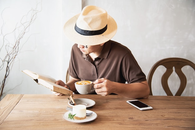 Asiatischer Mann, der einen Kaffee trinkt und ein Buch liest