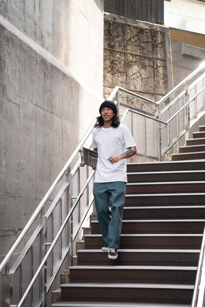 Asiatischer Mann, der sein Skateboard beim Gehen auf der Treppe hält