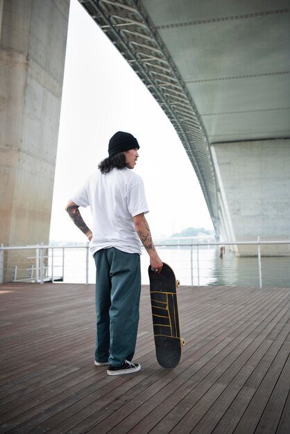 Asiatischer Mann, der sein Skateboard hält