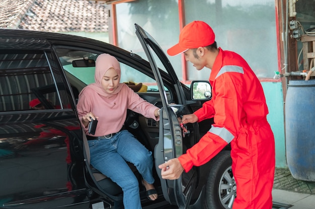 Asiatischer mann in roter uniform hilft, die tür zu öffnen, wenn ein kunde mit dem auto zur reparatur in die werkstatt kommt