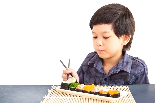 Asiatischer reizender Junge isst die Sushi, die über weißem Hintergrund lokalisiert werden