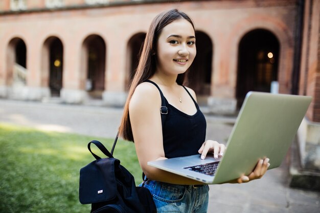 Asiatischer Student, der mit grünem Parkkonzept des Computerlaptops im Freien des Universitätscampus arbeitet