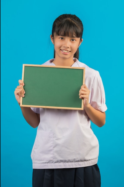 Asiatischer Student mit dem langen Haarmädchen, das ein grünes Brett auf einem Blau hält.