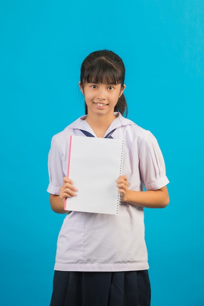 Asiatischer Student mit dem langen Haarmädchen, das ein Notizbuch auf einem Blau hält.