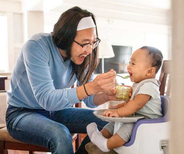 Asiatischer Vater füttert seinen kleinen Sohn mit Püree