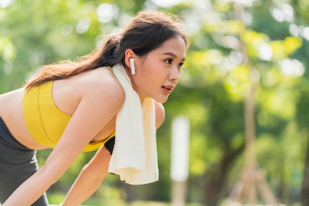 Asiatisches aktives weibliches Läufertraining, das nach einer Laufeinheit im Parkgarten gebeugt steht und zu Atem kommt Sportliche weibliche Frau, die nach einem Lauf im morgendlichen Übungslebensstil eine Pause einlegt