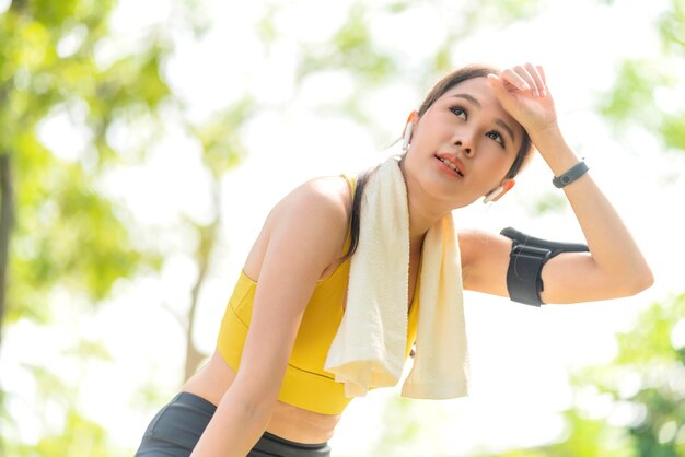 Asiatisches aktives weibliches Läufertraining, das nach einer Laufeinheit im Parkgarten gebeugt steht und zu Atem kommt Sportliche weibliche Frau, die nach einem Lauf im morgendlichen Übungslebensstil eine Pause einlegt