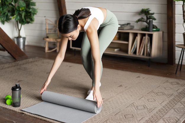 Asiatisches Fitness-Mädchen beendet das Training zu Hause rollende Bodenmatte nach Übungen im Wohnzimmer