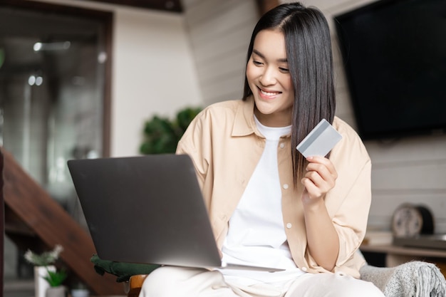 Asiatisches Mädchen, das für Online-Käufe mit Kreditkarte bezahlt, indem es Laptop auf der Website kauft