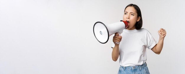 Asiatisches Mädchen, das Megaphon anschreit, junger Aktivist protestiert mit lauter Freisprecheinrichtung, die über weißem Hintergrund steht