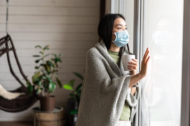 Asiatisches Mädchen mit Sehnsucht nach medizinischer Gesichtsmaske geht nach draußen, ist an Covid erkrankt und bleibt auf Selbstquara ...