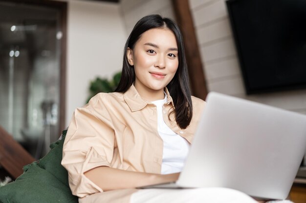 Asiatisches Mädchen sitzt im Wohnzimmer mit Laptop Frau schaut sich Videos auf dem Computer zu Hause an und entspannt sich mit ...