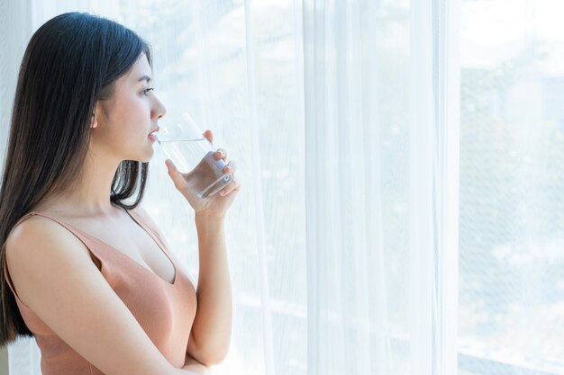 Asiatisches nettes Mädchen der schönen Schönheitsfrau fühlen sich glücklich, sauberes Getränkwasser für gute Gesundheit morgens trinkend