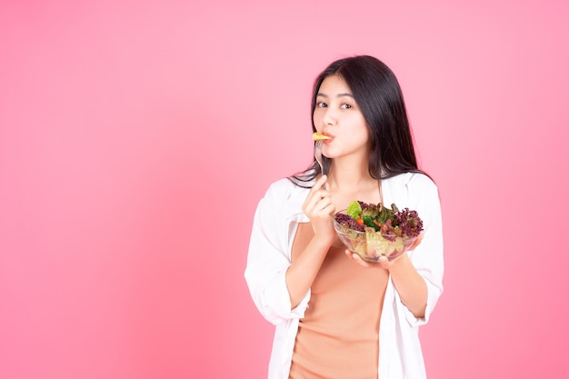 Asiatisches nettes Mädchen der Schönheitsfrau fühlen sich glücklich, frischen Salat des Diätlebensmittels für gute Gesundheit auf rosa Hintergrund essend