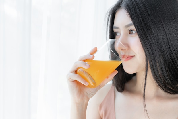 Asiatisches nettes Mädchengefühl der schönen Schönheitsfrau glücklich, Orangensaft für gute Gesundheit morgens trinkend