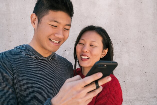 Asiatisches Paar, das das Handy betrachtet.