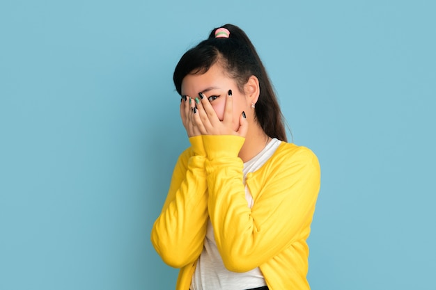 Asiatisches Teenagerporträt lokalisiert auf blauem Studiohintergrund. Schönes weibliches brünettes Modell mit langen Haaren im lässigen Stil. Konzept der menschlichen Emotionen, Gesichtsausdruck, Verkauf, Anzeige. Positiv posieren.