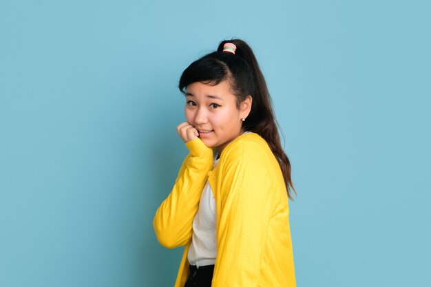 Asiatisches Teenagerporträt lokalisiert auf blauem Studiohintergrund. Schönes weibliches brünettes Modell mit langen Haaren im lässigen Stil. Konzept der menschlichen Emotionen, Gesichtsausdruck, Verkauf, Anzeige. Positiv posieren.