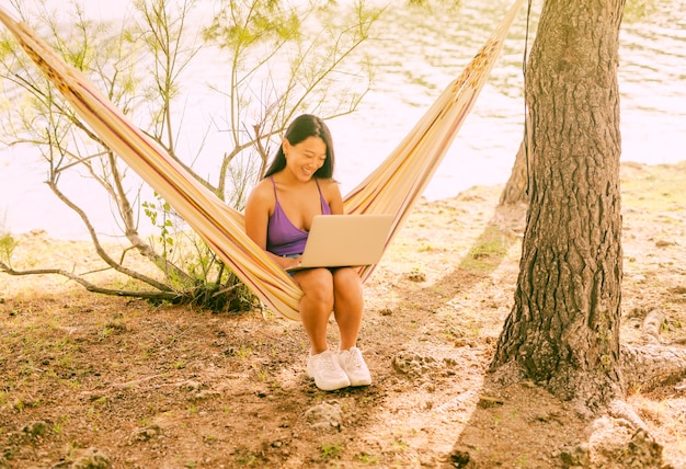 Kostenloses Foto asiatisches weibliches sitzen in der hängematte mit laptop und dem lächeln