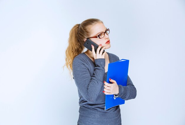 Assistent mit Brille hält einen blauen Ordner und spricht mit dem Telefon.