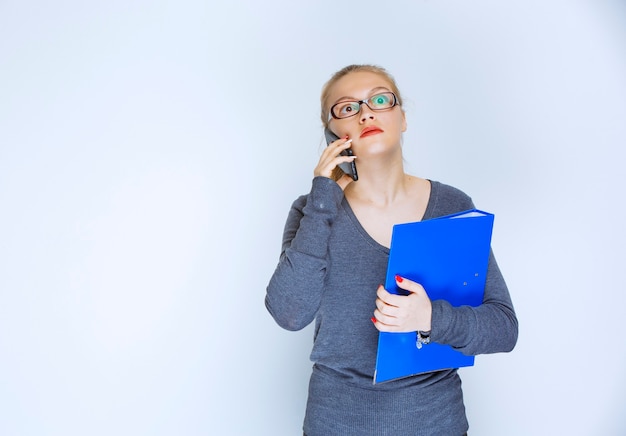 Assistent mit brille hält einen blauen ordner und spricht mit dem telefon.