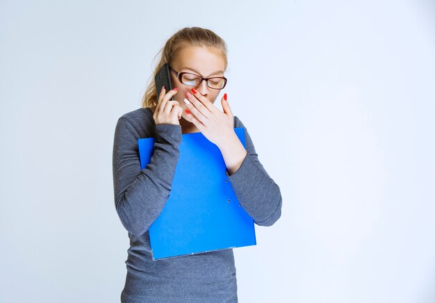 Assistent mit Brille hält einen blauen Ordner und spricht mit dem Telefon.