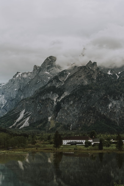 Atemberaubende aufnahme des braunen und weißen hauses in der nähe des sees und der berge unter einem bewölkten himmel