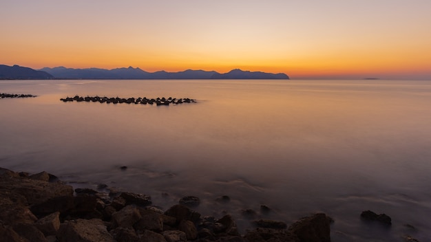 Atemberaubende Aufnahme des ruhigen Meeres und des felsigen Ufers während des Sonnenuntergangs