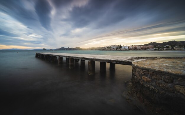 Atemberaubende Aussicht auf die Seelandschaft mit einem hölzernen Pier am malerischen dramatischen Sonnenuntergang